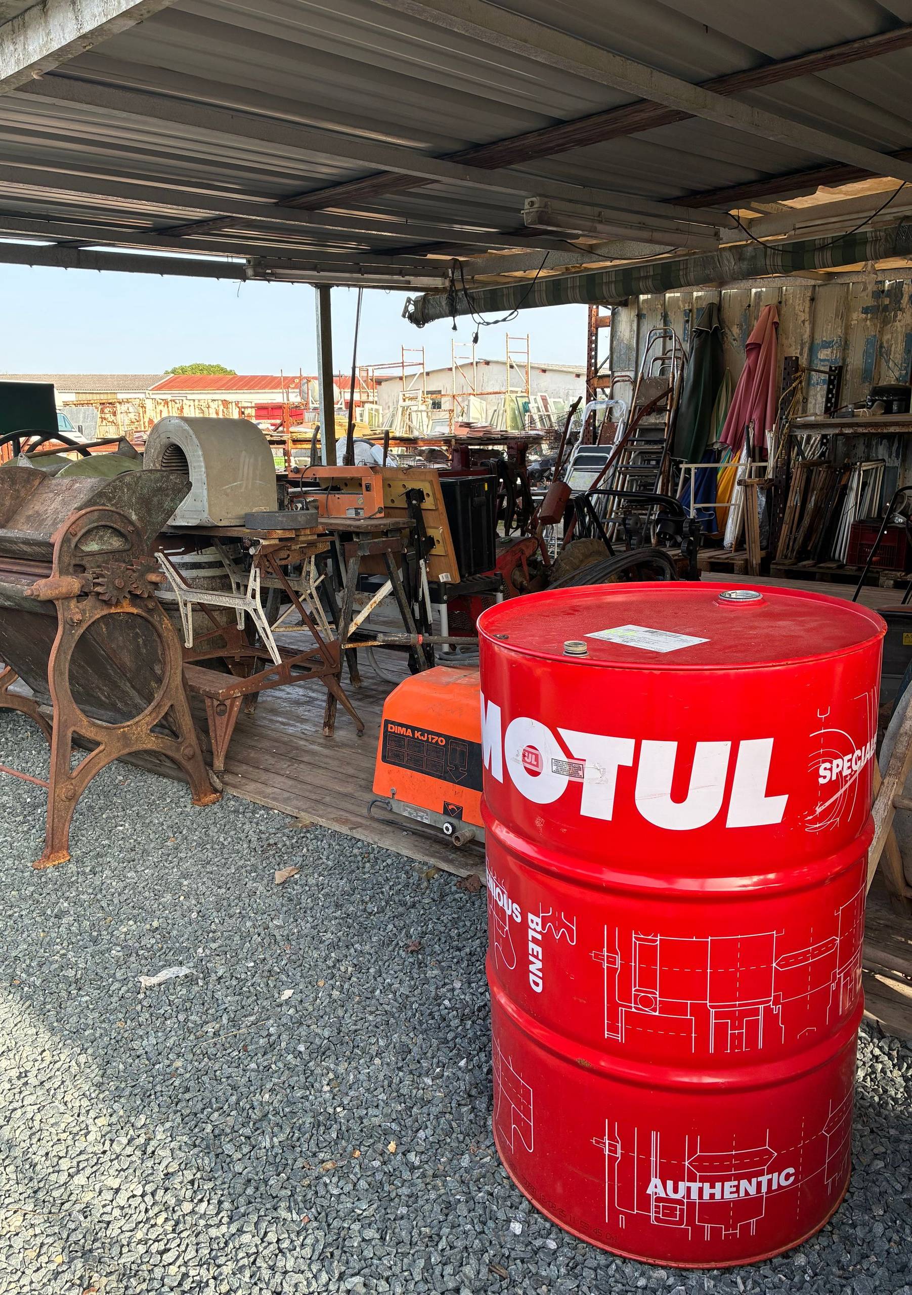 Un fût d'huile Motul rouge dans un hangar métallique avec des machines rouillées.