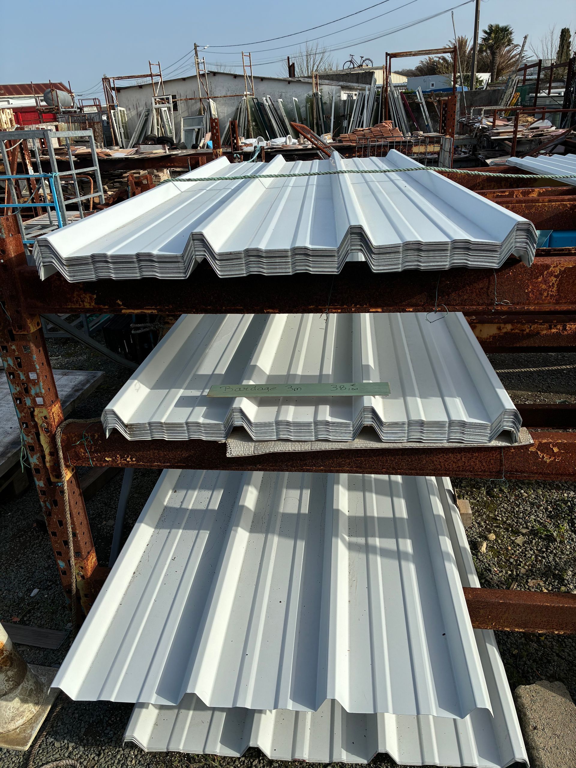 Des plaques de toiture en tôle ondulée empilées sur des étagères à l'extérieur.
