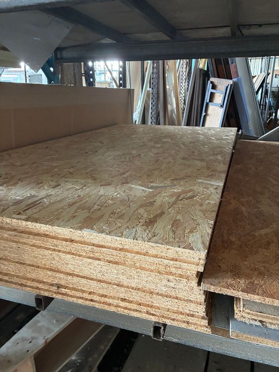 Pile de panneaux de particules orientées (OSB), vue d'un angle légèrement inférieur, stockée sur des étagères métalliques.