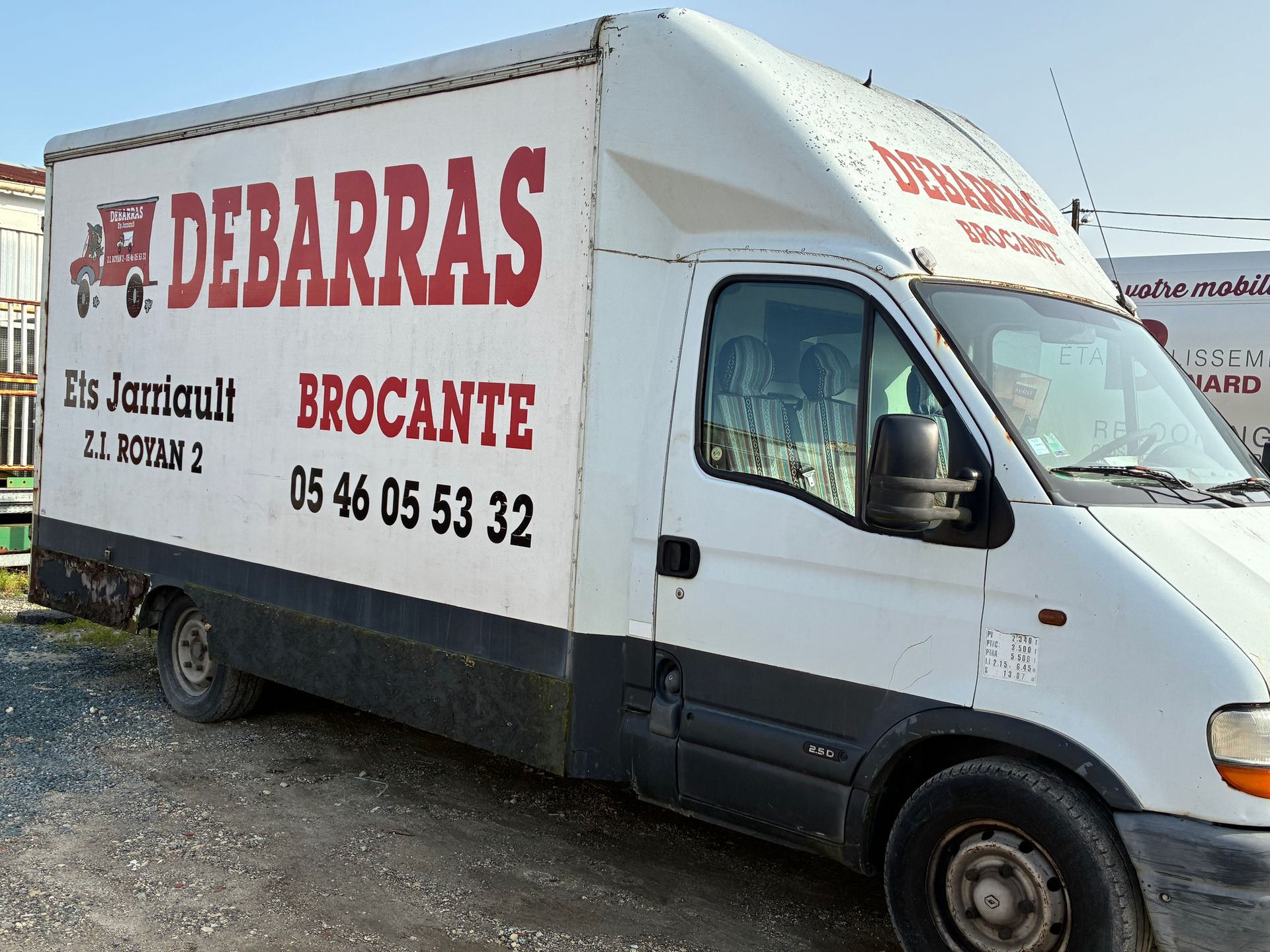 Camionnette de livraison blanche, stationnée à l'extérieur. Un numéro de téléphone est inscrit en noir.