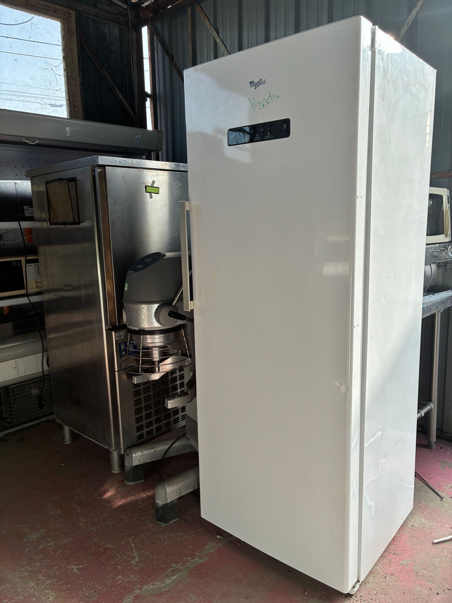 Un grand congélateur blanc Whirlpool se dresse à côté d'un appareil électroménager en acier inoxydable dans un intérieur encombré.