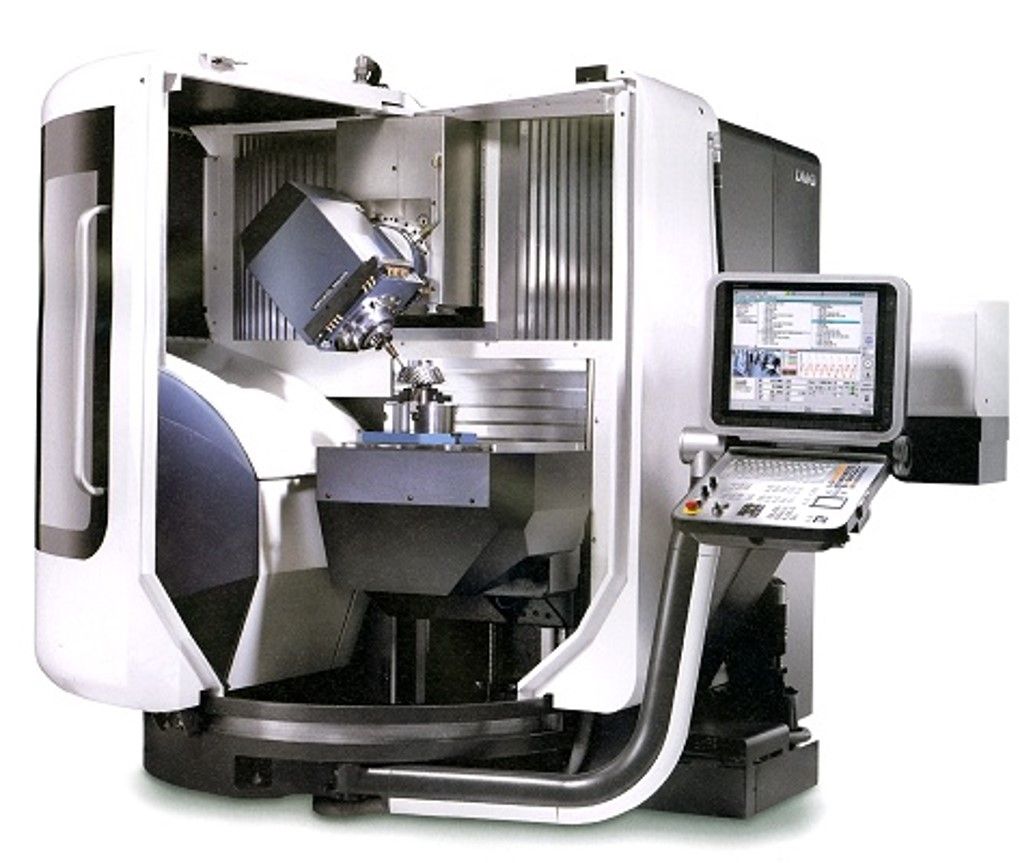 Máquina CNC, gris y blanca, visible. Se mecaniza una pieza en su interior. Pantalla de ordenador visible.