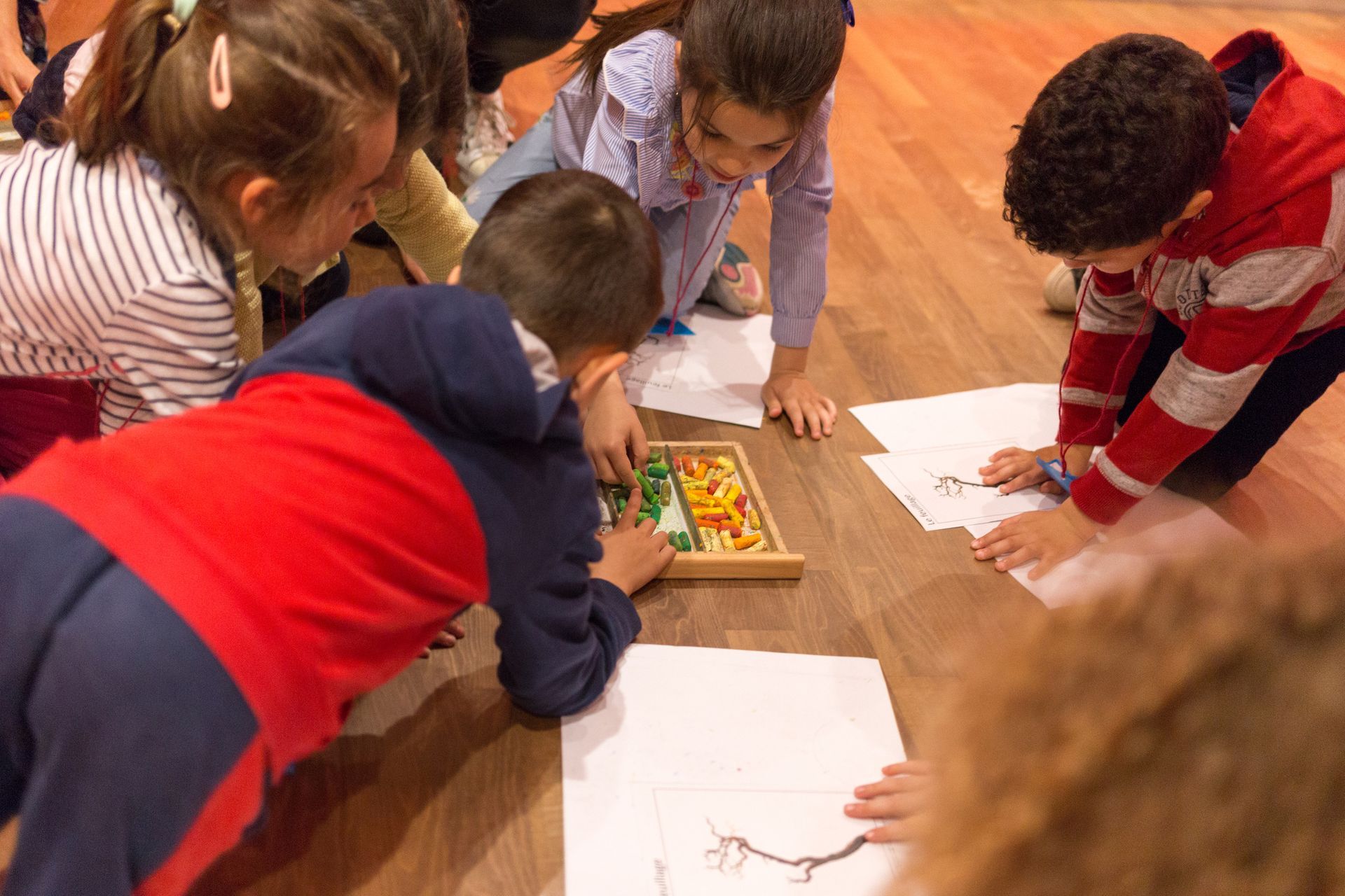 Niños en el suelo, dibujando y jugando con piezas de madera de colores sobre papel.
