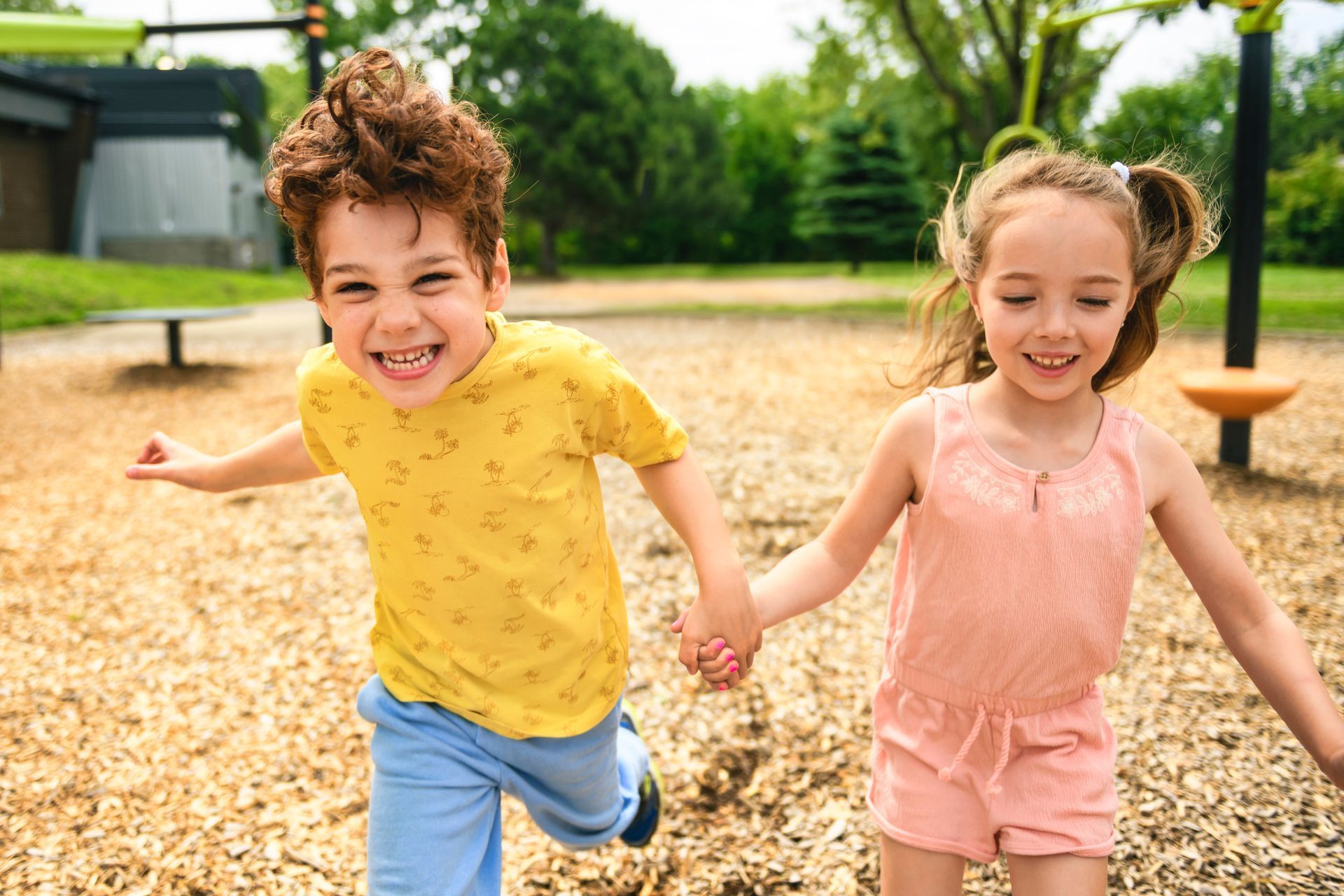 Dos niños corriendo y tomados de la mano en un patio de recreo, sonriendo.