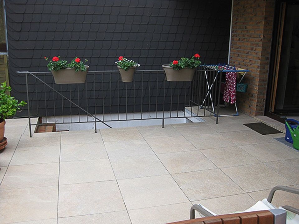 Ein Balkon mit Geländer und Pflanzkübeln mit roten Blumen Scharwat - Fliesen und Naturstein