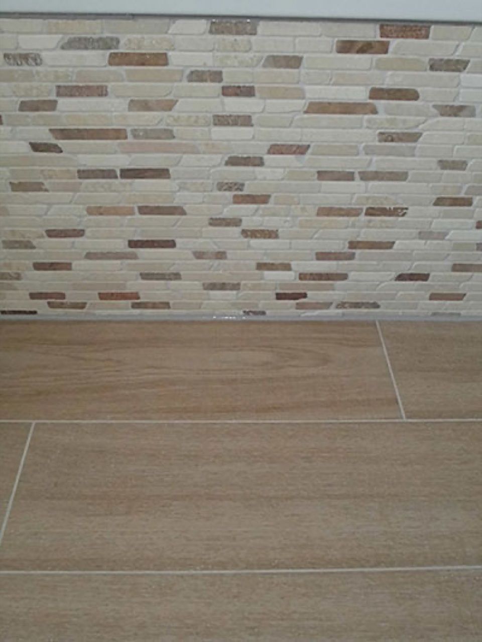 Eine geflieste Wand mit einem Holzboden davor. Scharwat - Fliesen und Naturstein