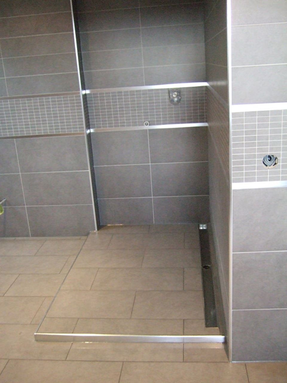 Ein Badezimmer mit grauen Fliesen und einer ebenerdigen Dusche Scharwat - Fliesen und Naturstein