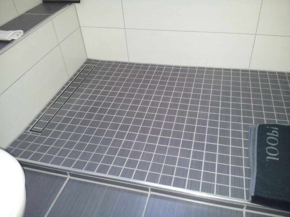 Ein Badezimmer mit gefliestem Boden und einer Toilette Scharwat - Fliesen und Naturstein