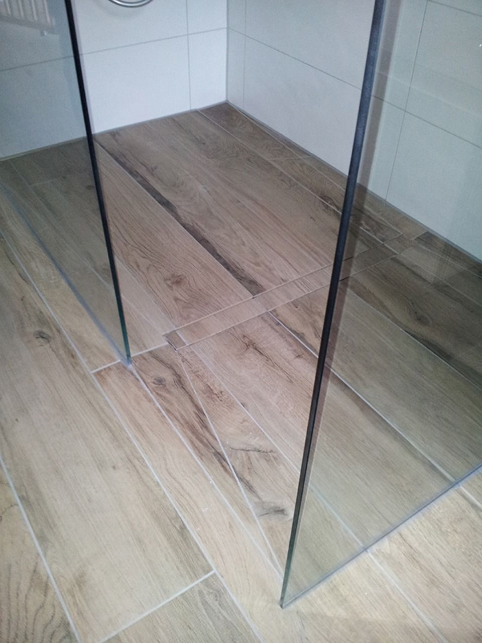 Eine ebenerdige Dusche mit Holzboden und Glastür. Scharwat - Fliesen und Naturstein