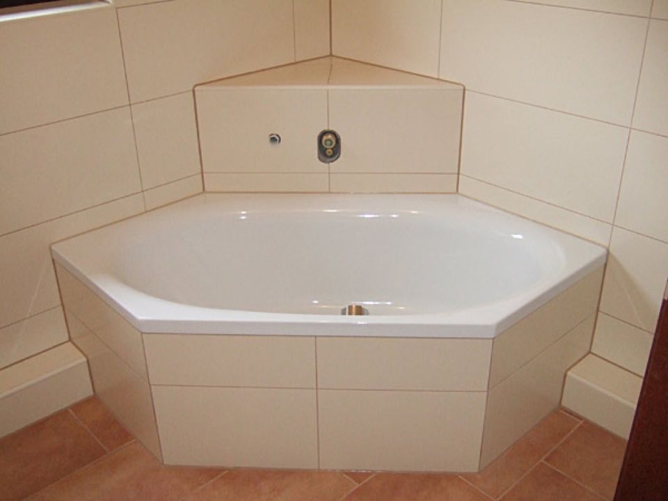 Eine weiße Badewanne steht in der Ecke eines Badezimmers Scharwat - Fliesen und Naturstein