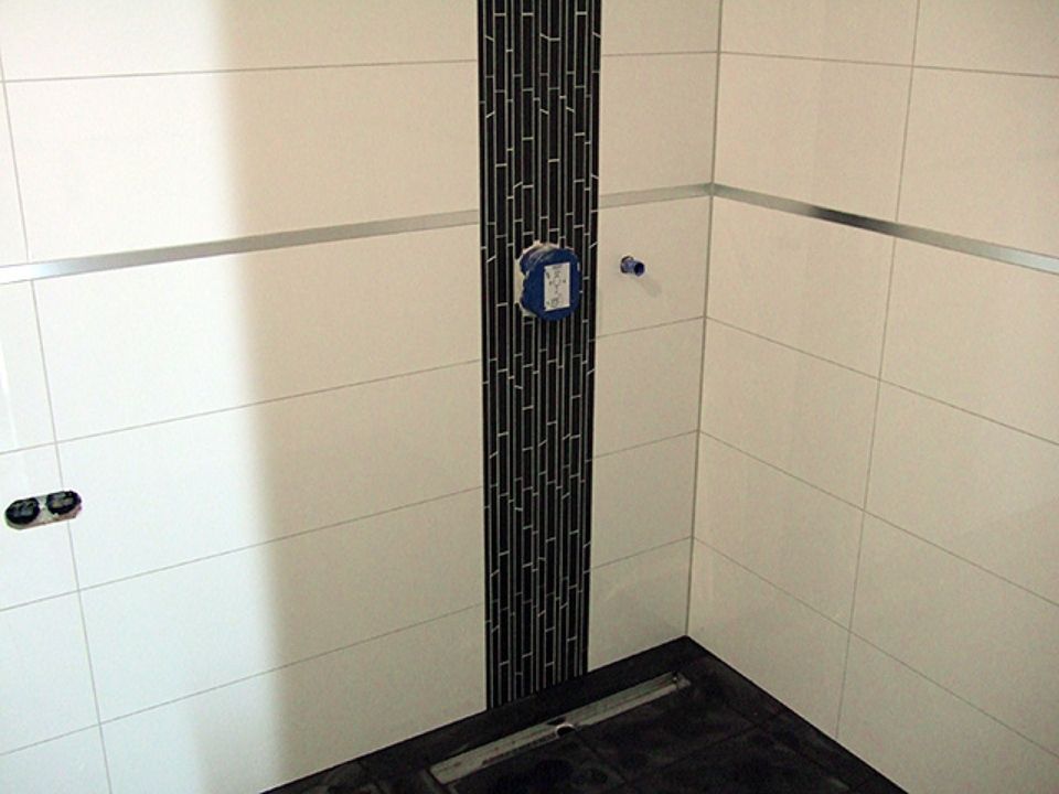 Ein Badezimmer mit weißen Fliesen und schwarzen Streifen an der Wand Scharwat - Fliesen und Naturstein