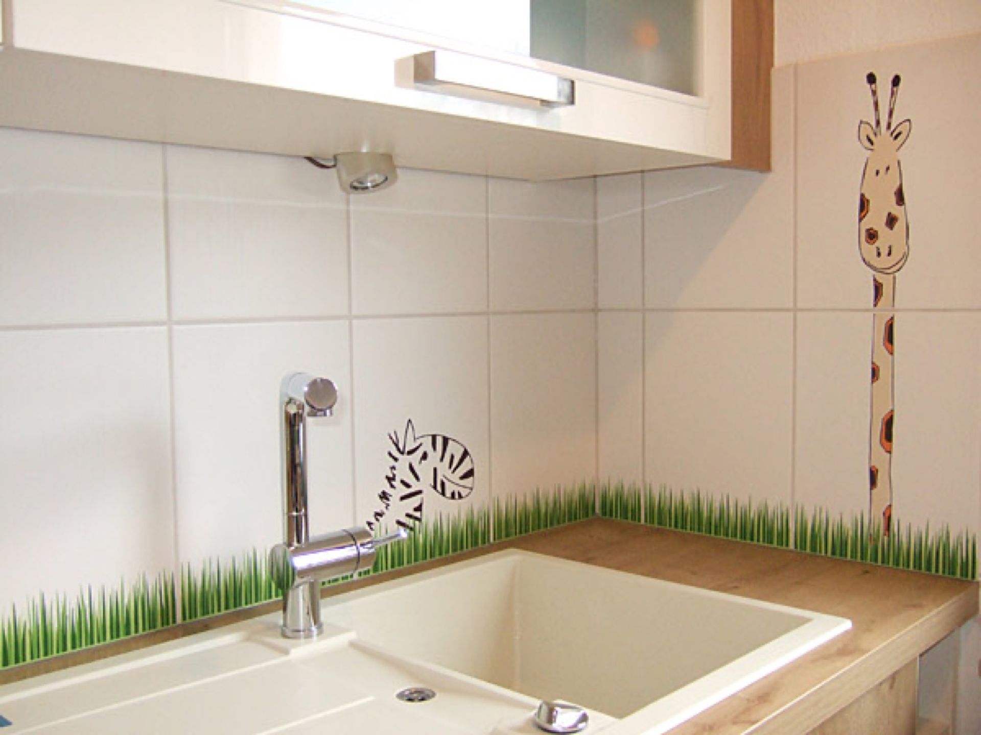 Eine Küchenspüle mit einer Giraffe an der Wand dahinter, Scharwat - Fliesen und Naturstein
