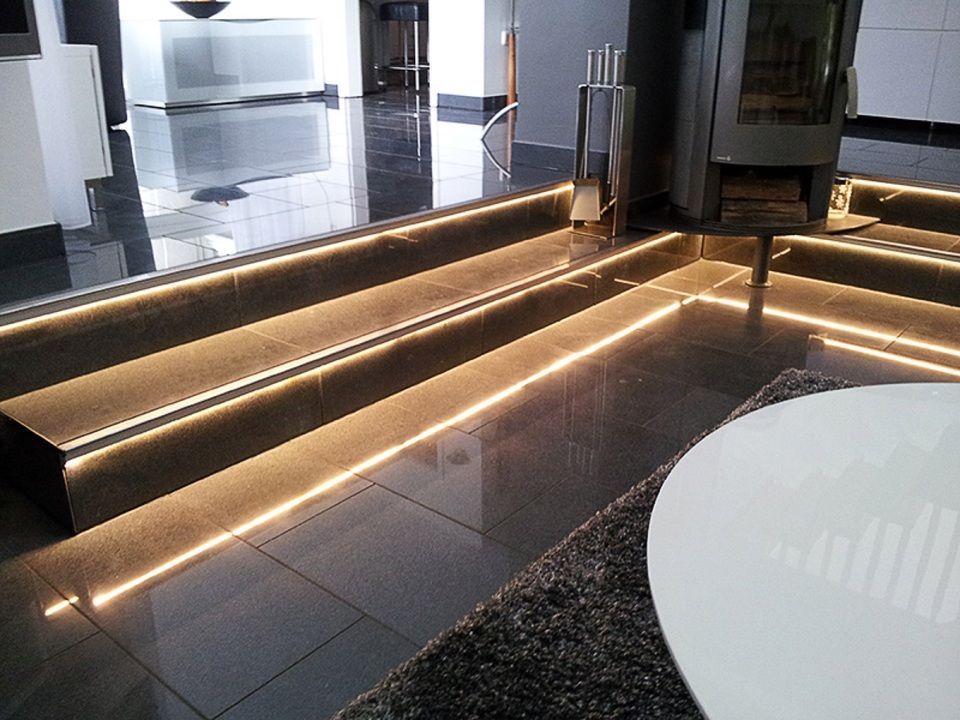 Ein Wohnzimmer mit Kamin und beleuchteter Treppe Scharwat - Fliesen und Naturstein