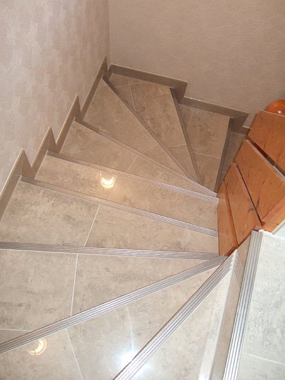 Eine Wendeltreppe mit einem Metallgeländer und einem Holzhandlauf Scharwat - Fliesen und Naturstein