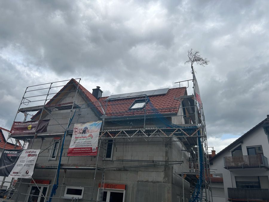 Ein im Bau befindliches Gebäude mit Gerüst, rotem Ziegeldach und bewölktem Himmel.