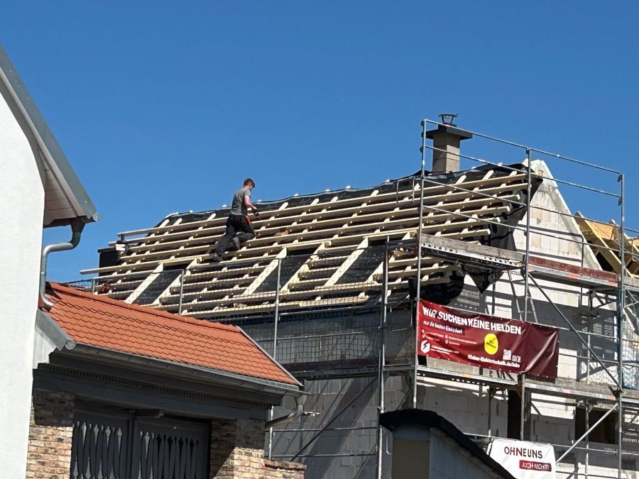 Ein Dachdecker arbeitet an einem im Bau befindlichen Haus; Gerüst, strahlend blauer Himmel.