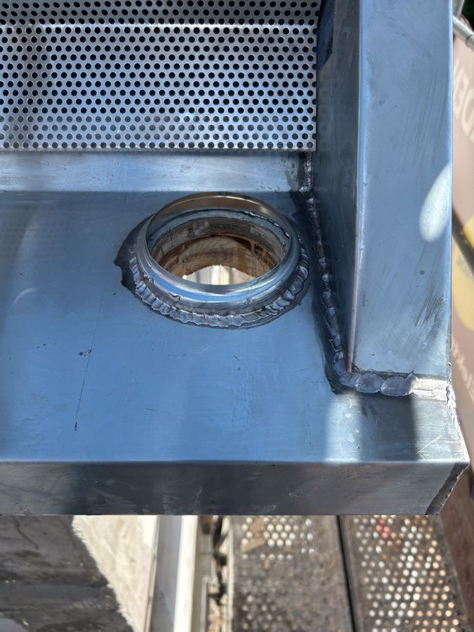 Nahaufnahme eines Edelstahlspülbeckens mit einer runden, geschweißten Öffnung und einem perforierten Metallabschnitt.