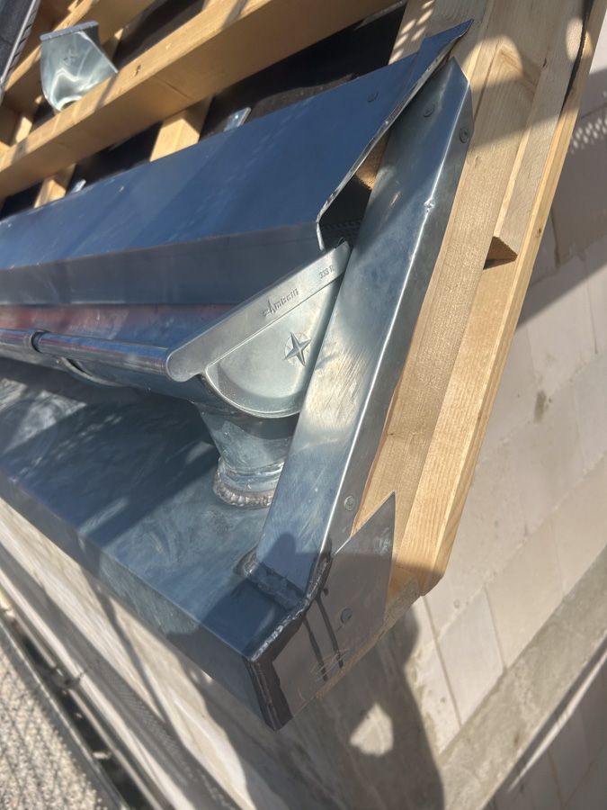 Eine verzinkte Metallrinne ist auf einem Dach mit einem Fallrohr an der Ecke installiert.