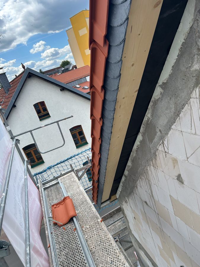 Die Errichtung eines Gebäudedachs mit roten Ziegeln, Gerüst und Dachrinne vor dem Hintergrund eines weißen Gebäudes.