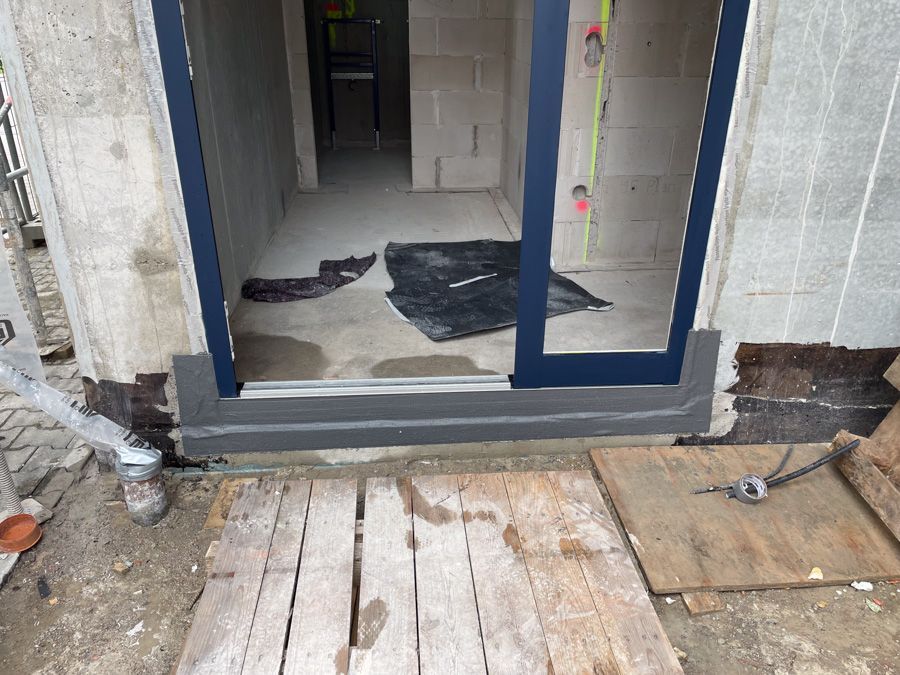 Im Bau befindliche Außentür mit dunkelblauem Rahmen und grauer Schwelle. Darunter befinden sich Holzplanken.