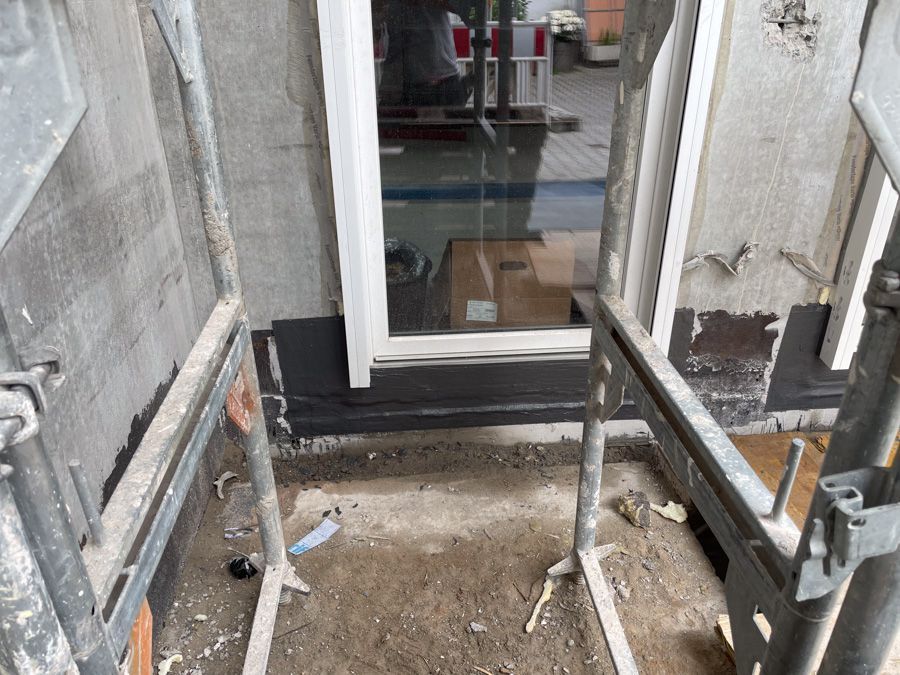 Ein Gerüst umgibt ein Fenster an einem Gebäude; unterhalb des Fensterrahmens ist schwarzes Blech sichtbar.