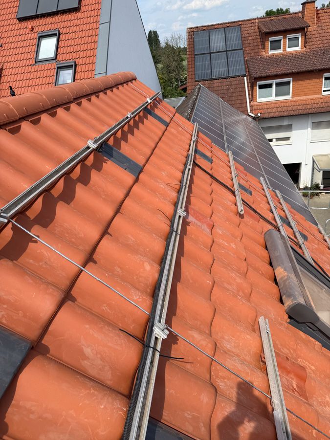 Das Dach ist mit roten Ziegeln gedeckt und mit Solarmodulen ausgestattet. Silberne Metallgeländer und Tragkonstruktionen sind sichtbar.