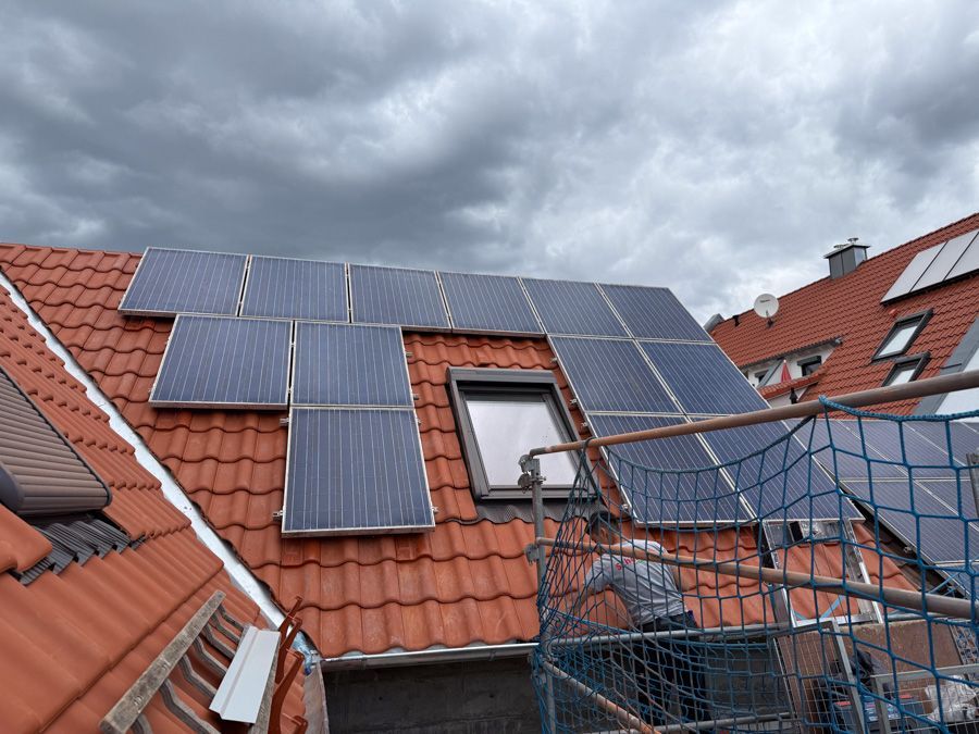 Solarpaneele auf einem rotziegelgedeckten Dach mit Oberlicht; darüber bewölkter Himmel.
