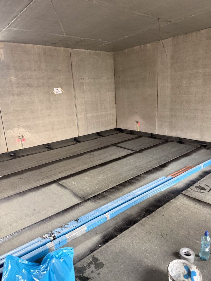 Ein im Bau befindlicher Raum mit grauen Wänden und Boden, blauen Rohren.