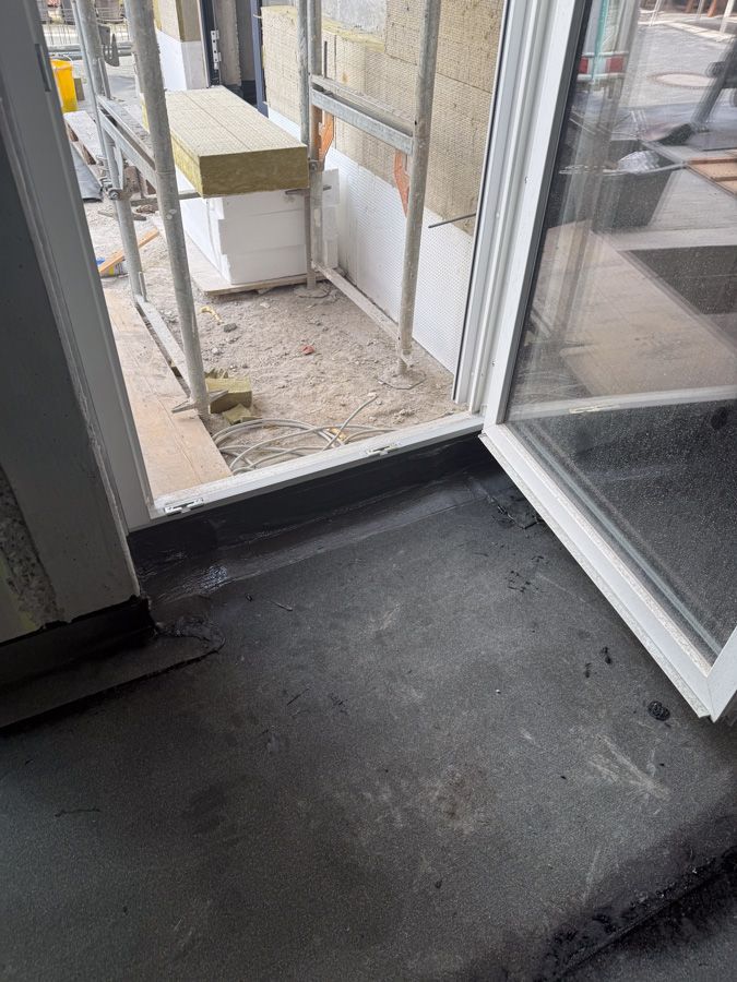 Eingangsbereich mit dunklem Boden und unfertiger Baustelle. Weißer Türrahmen.