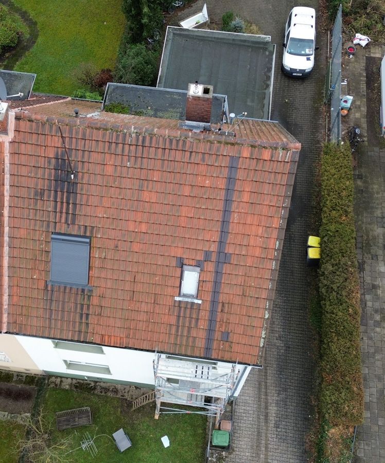 Draufsicht auf ein Haus mit rotem Ziegeldach, einen weißen Lieferwagen und eine grüne Hecke.