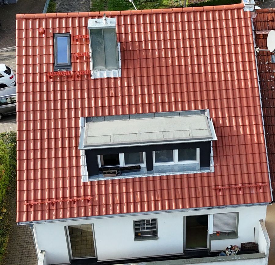 Das rotziegelgedeckte Dach eines Hauses mit mehreren Fenstern und einer kleinen Dachgaube.