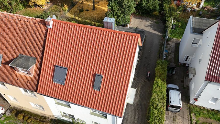 Luftaufnahme von Häusern mit orangefarbenen Ziegeldächern und einem weißen Lieferwagen, der in der schmalen Straße darunter parkt.