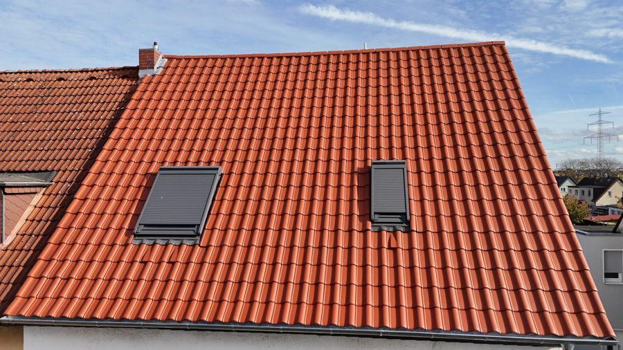 Rotes Ziegeldach mit zwei dunklen Oberlichtern unter blauem Himmel.