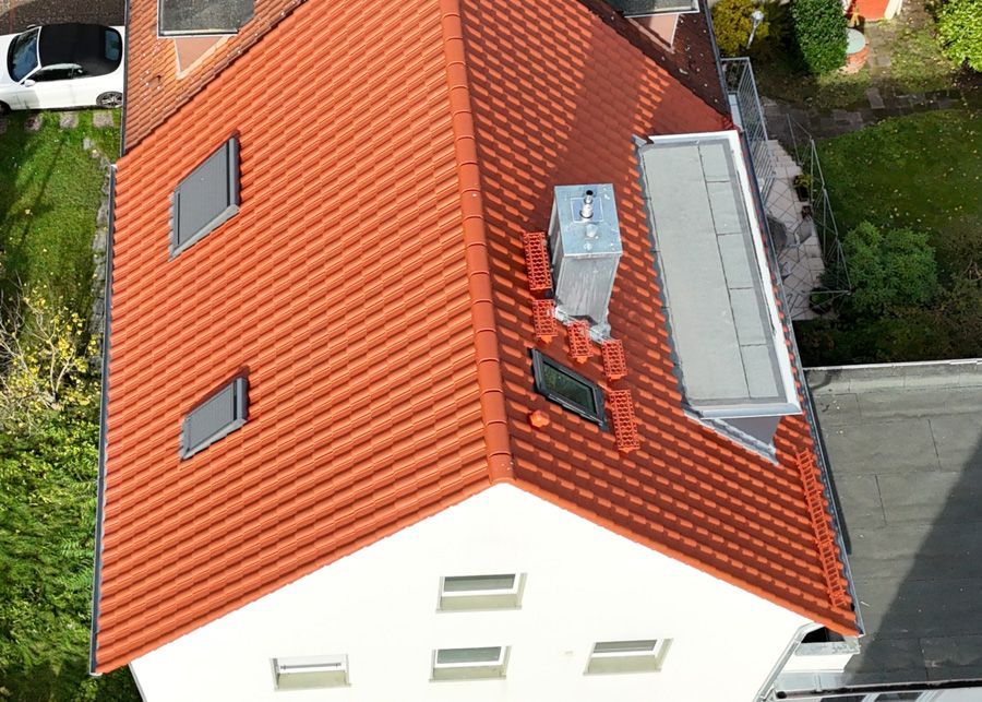 Luftaufnahme eines Hauses mit rotem Ziegeldach, Oberlichtern und Schornstein.