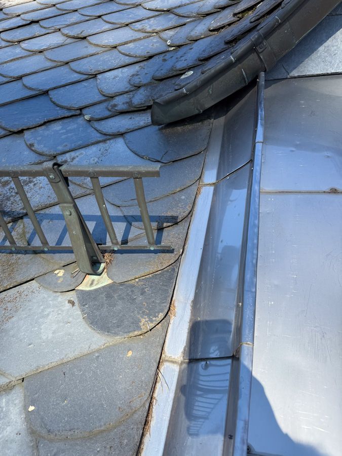 Schieferdach mit Dachrinne und Metallgeländer.