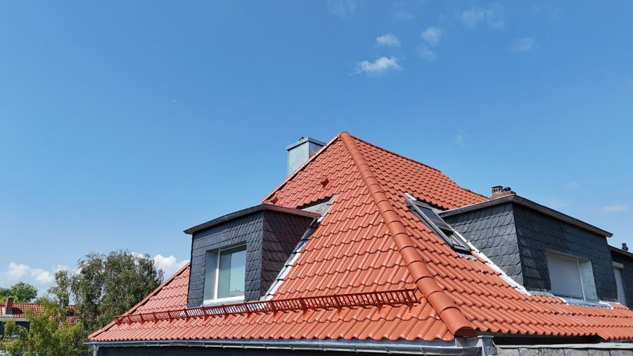 Ein rot gedecktes Ziegeldach mit Dachgauben vor blauem Himmel.