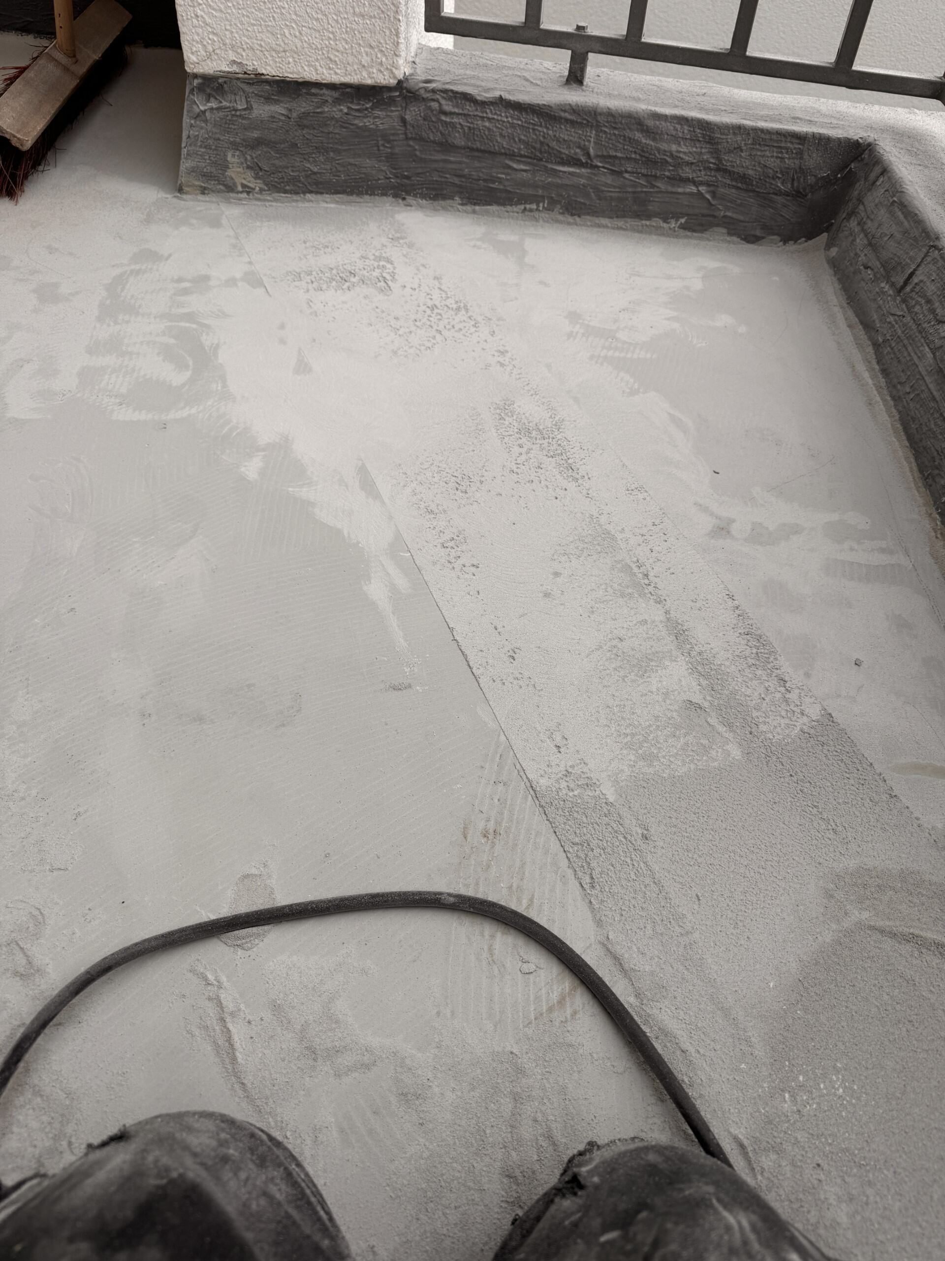 Betonierte Terrassenfläche mit einer Steinstufe und einem schwarzen Schlauch im Vordergrund