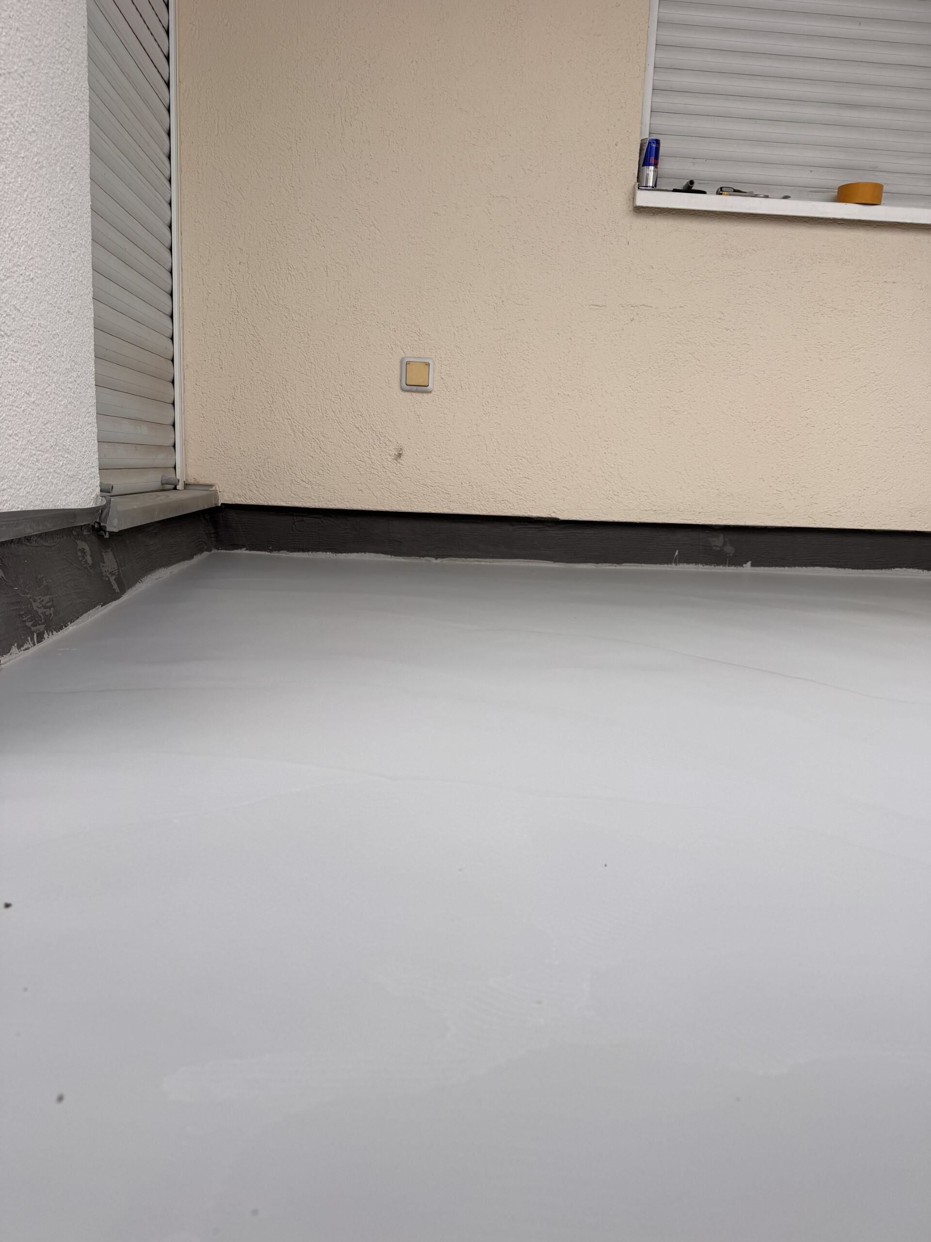 Leerer Raum mit hellgrauem Boden, beigen Wänden und einer weißen Tafel auf der rechten Seite.
