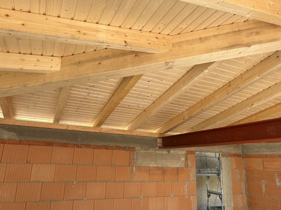 Holzbalken an der Decke über einer unfertigen Ziegelinnenwand mit einer Türöffnung