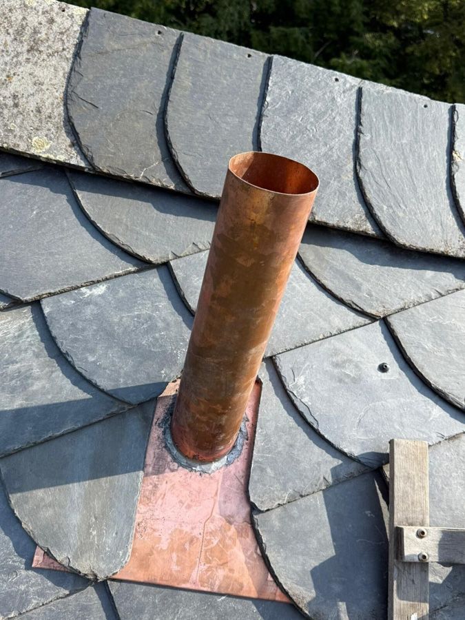 Kupfernes Dachlüftungsrohr auf einem Schieferdach mit reparierter Dacheindeckung.