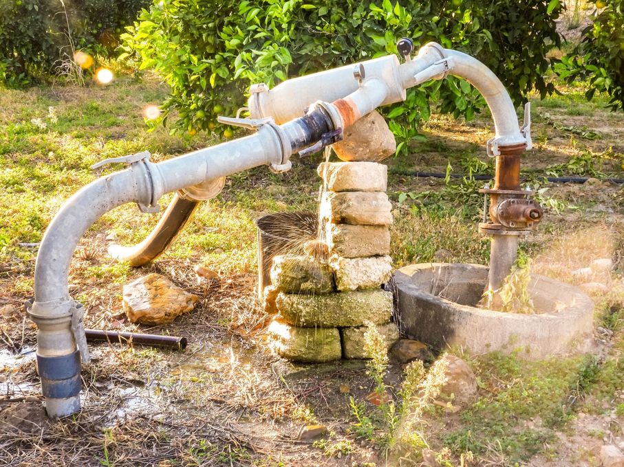 Bomba de agua de pozo en un entorno exterior soleado, bombeando agua a un recipiente.