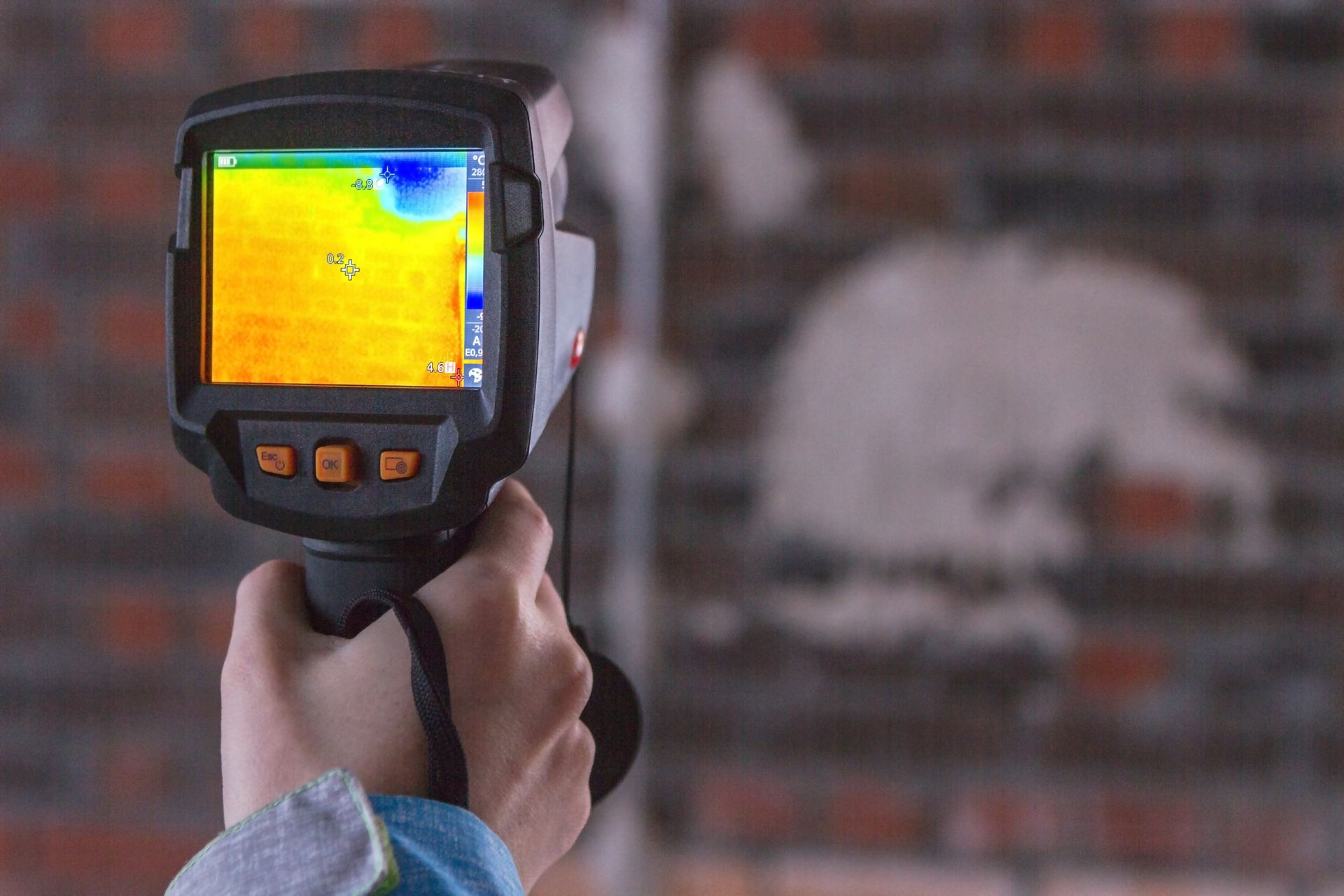 Persona que utiliza una cámara térmica y muestra la firma de calor en una pared de ladrillos.