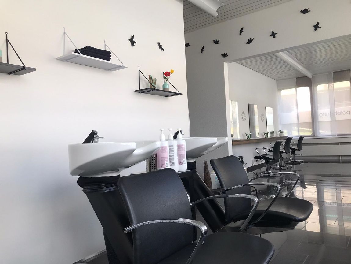 Modernes Saloninterieur mit schwarzen Friseurstühlen, Spiegeln und Wandregalen an einer weissen Wand