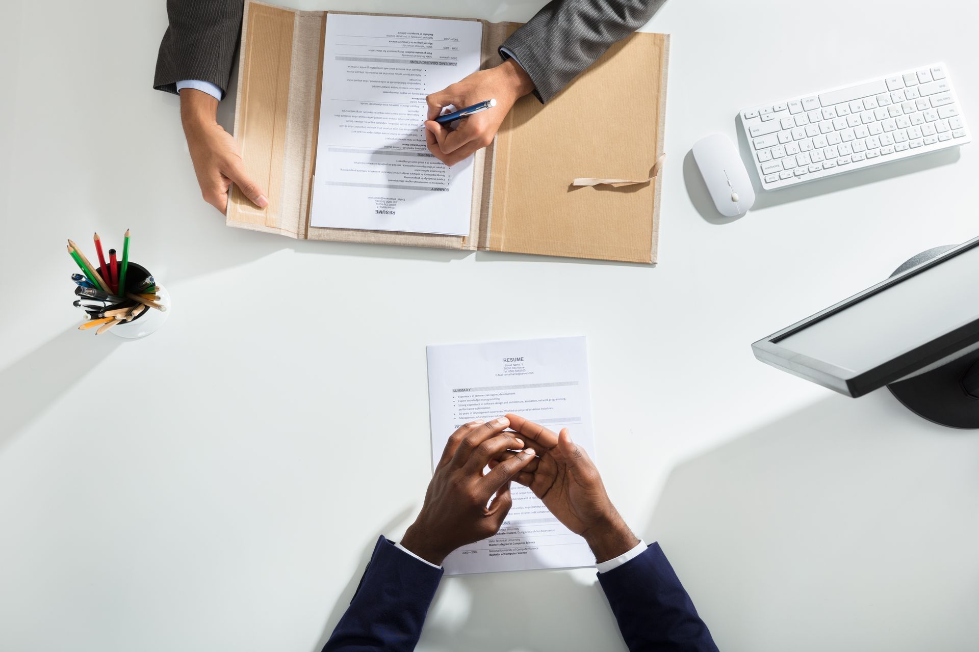 Deux personnes à un bureau avec des documents sur un bureau blanc, un stylo et un clavier à proximité.