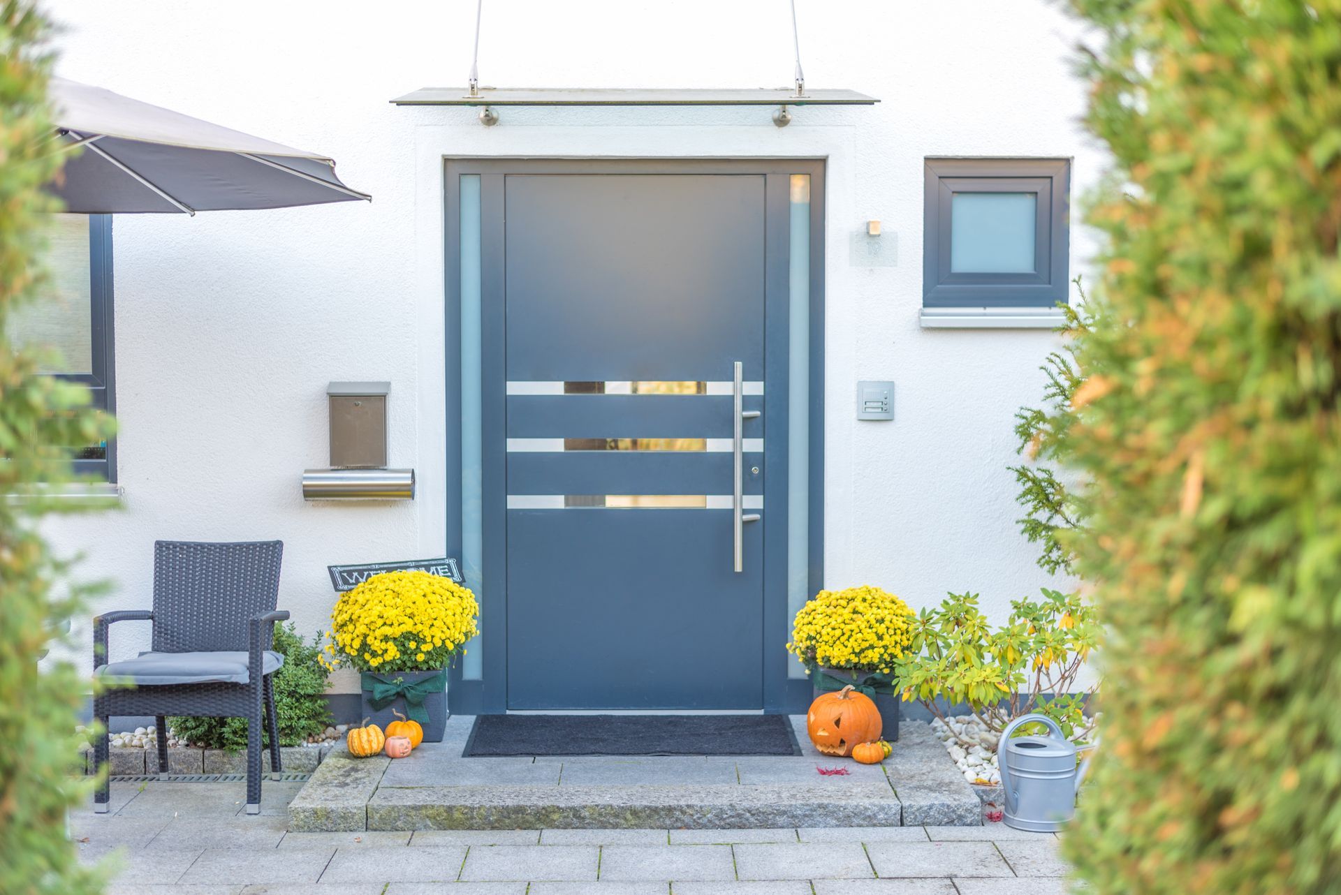 Porte d’entrée moderne avec des encadrements bleu-gris, des fleurs jaunes et une petite chaise de patio dans une entrée bien rangée