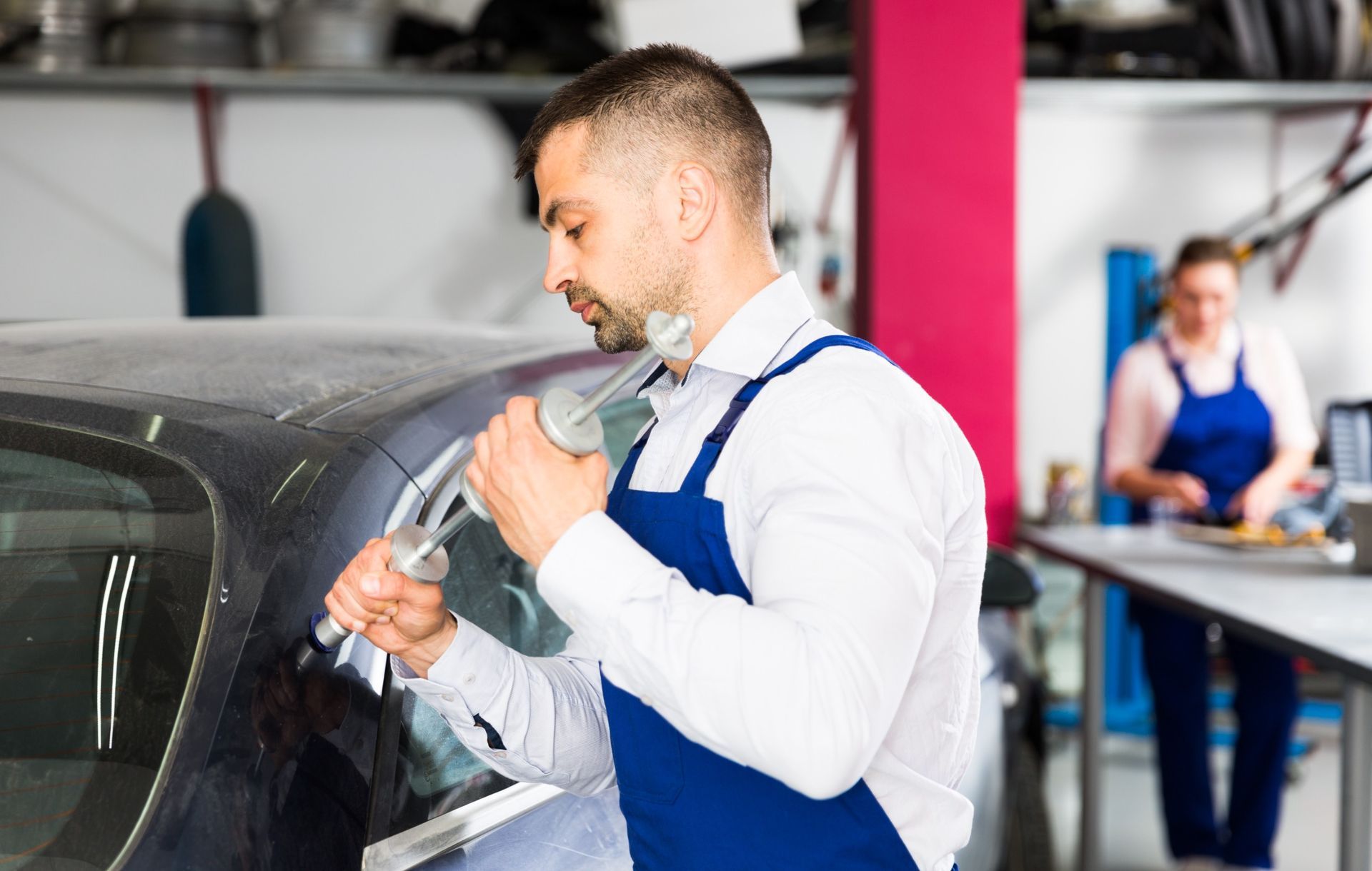Un hombre está trabajando en el parabrisas de un automóvil en un garaje.