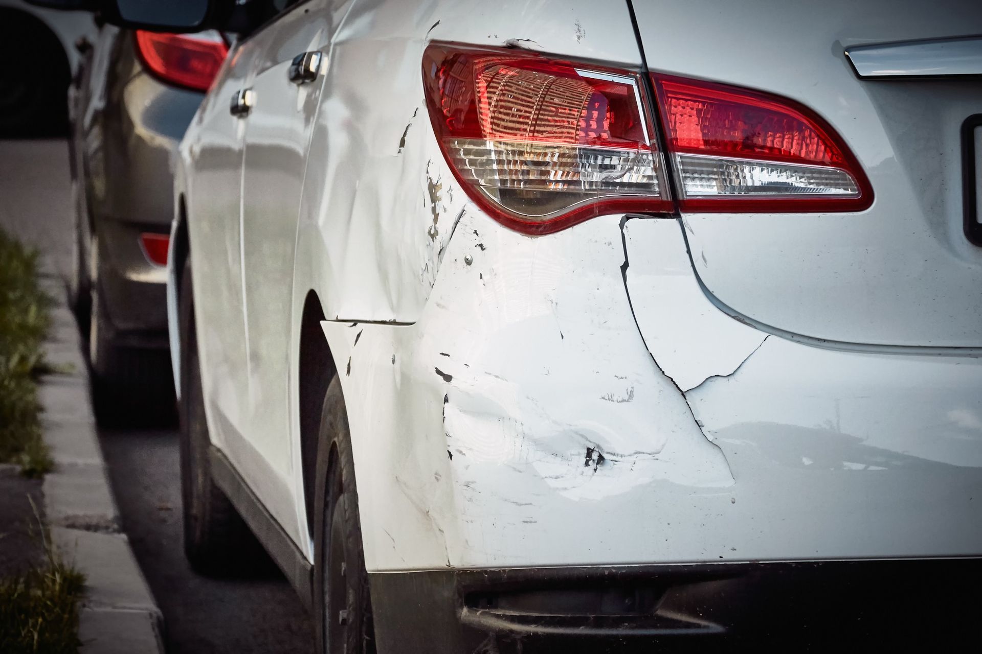 Un coche blanco con el parachoques dañado está estacionado al costado de la carretera.