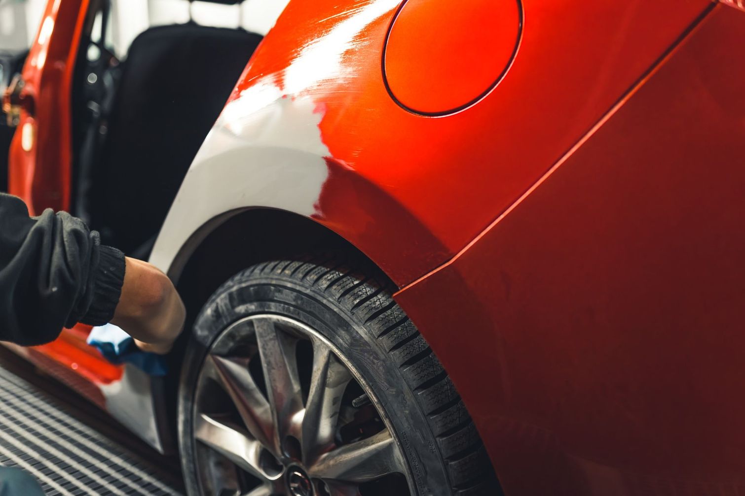 Un hombre está pintando el costado de un automóvil rojo.