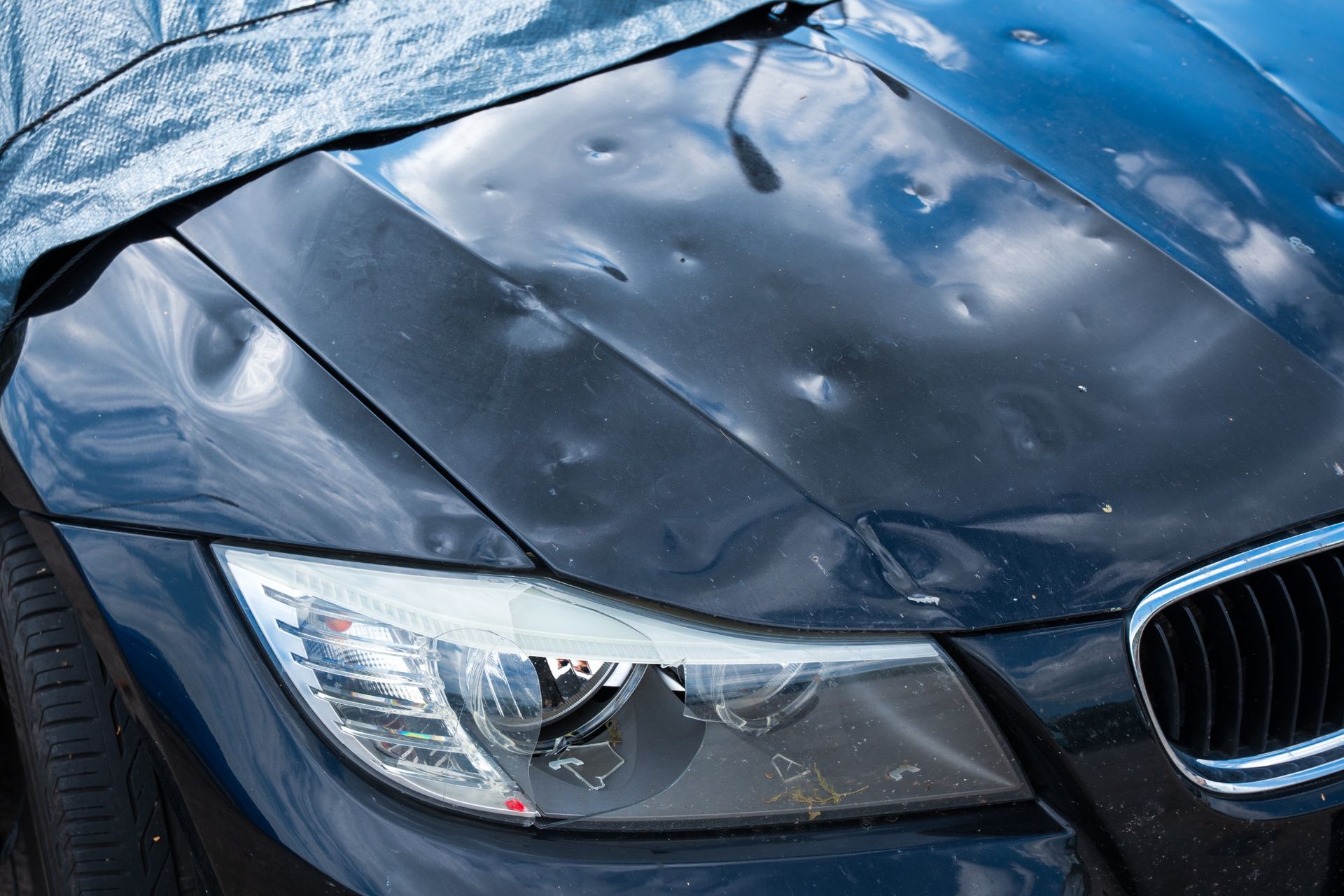 Un primer plano de un automóvil azul con daños por granizo en el capó.