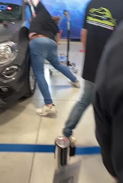 Una mujer está apoyada contra un coche en una sala de exposición.